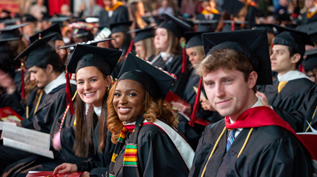  A group photo of La Roche University students in their caps and gowns attending the graduation ceremony at La Roche. Three of them are smiling at the camera.