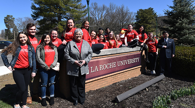 Sister Candace along with students gather around our sign celebrating our change to University status