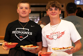 Two La Roche University students wearing Redhawk shirts holding plates of food in the Cantellops Dining Hall.