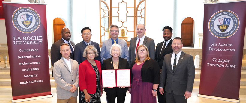 A group of 10 people posing for a picture dressed in business attire. The person in the center is holding a certificate.